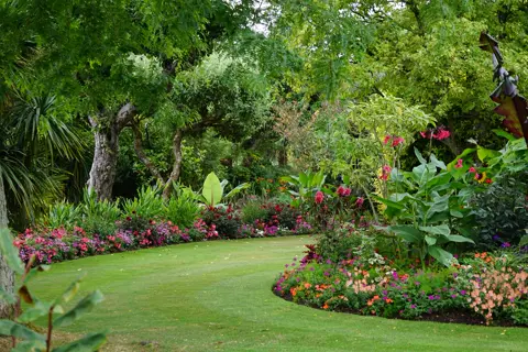 Een tuin met gazon en borders vol bloemen.